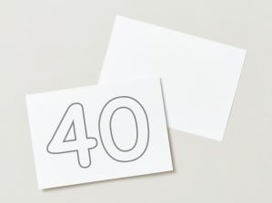 Image: two pieces of white paper laying on a table. One of the pieces of paper shows the number 40 in bubble writing, ready for colouring in.